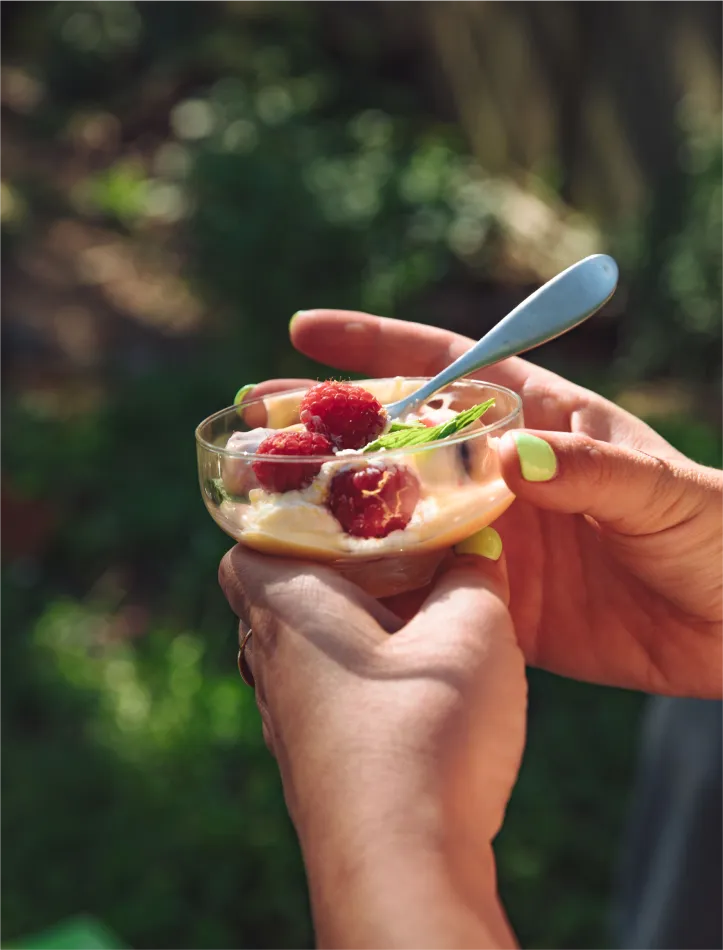 Hands with green painted nails holding a raspberry dessert.