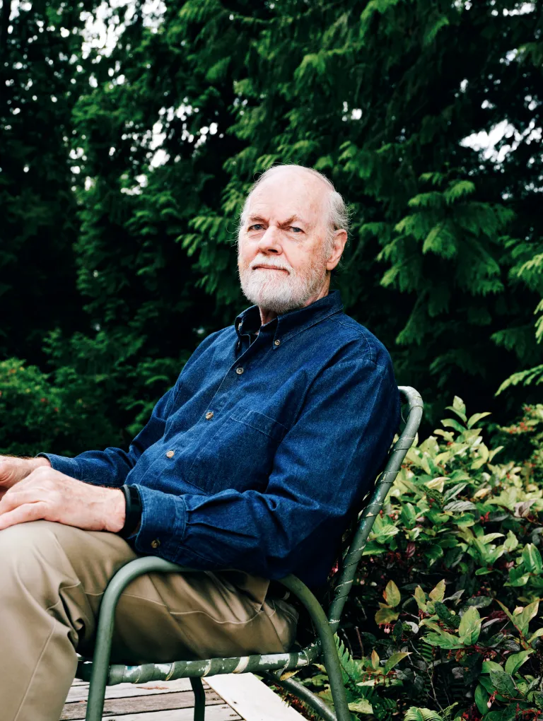 Portrait of an older gentleman in a blue shirt sitting in his garden.