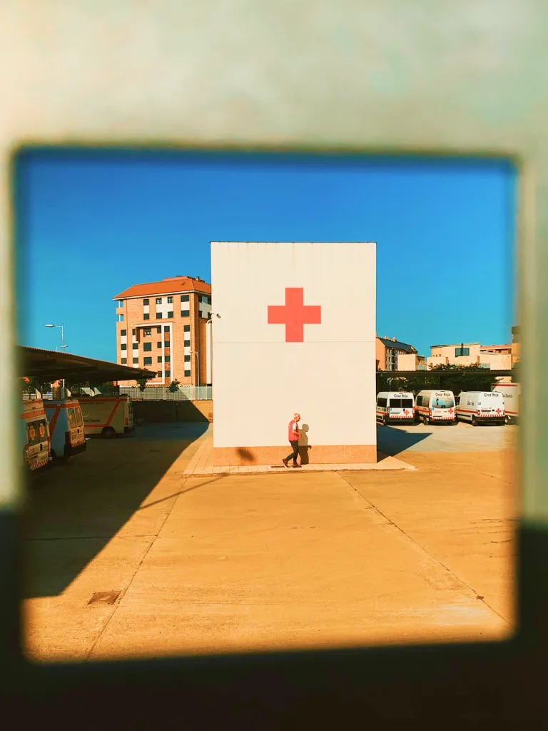 Medium distance shot of a person walking in front of a wall with a red cross on it on a sunny day.
