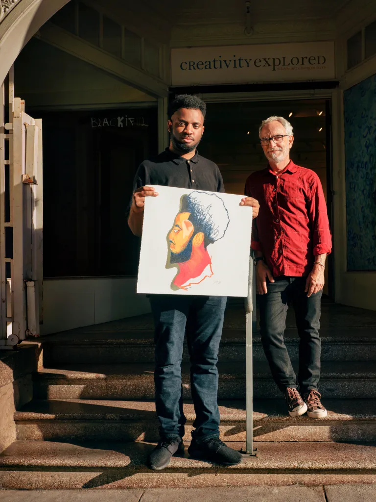 Two people standing in front of a store holding holding a painting.